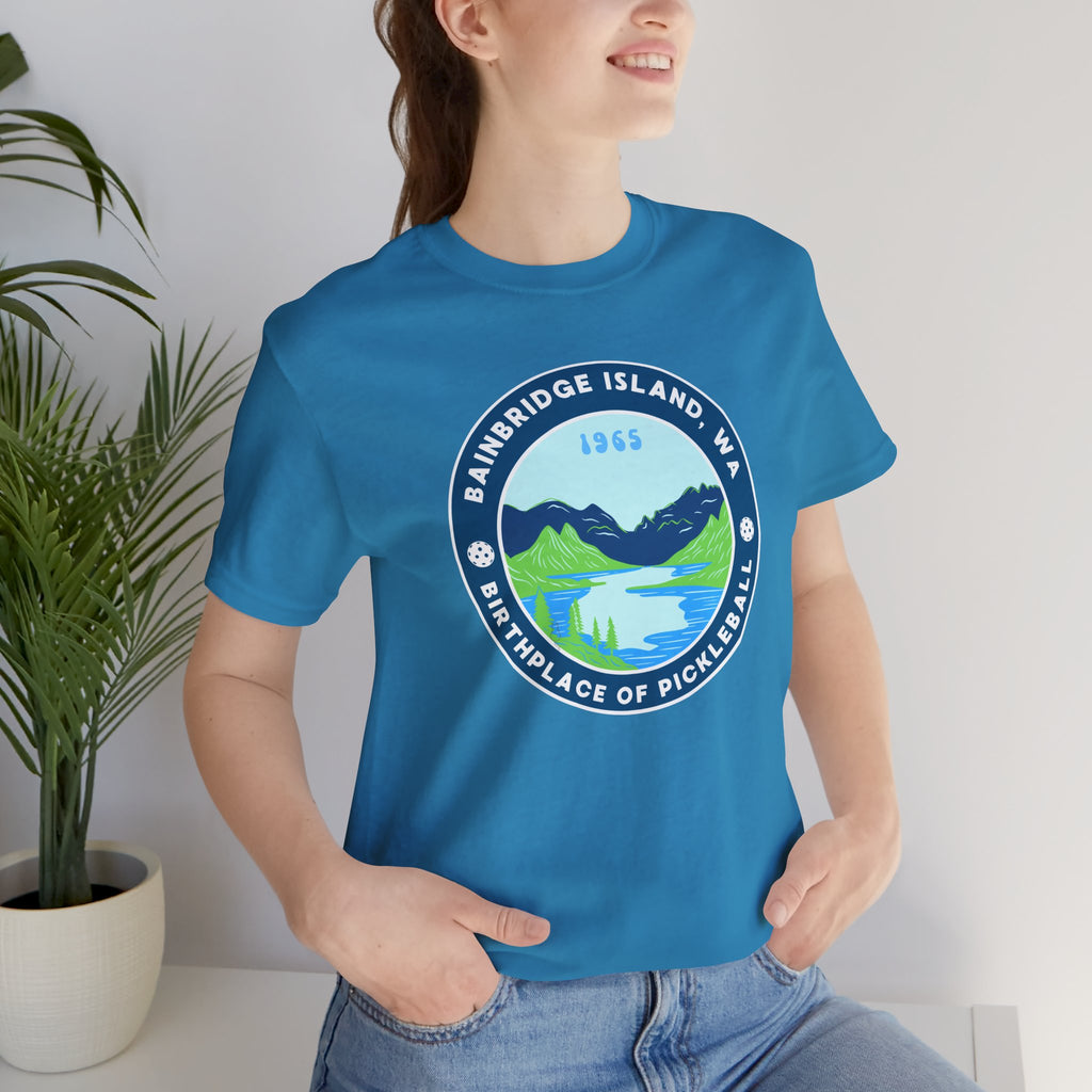 Unisex Bainbridge Island Pickleball T-Shirt featuring "Birthplace of Pickleball 1965" logo on white fabric.