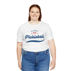 Red and blue pickleball T-shirt with script logo and paddle and ball graphic, casual printify design for pickleball players.