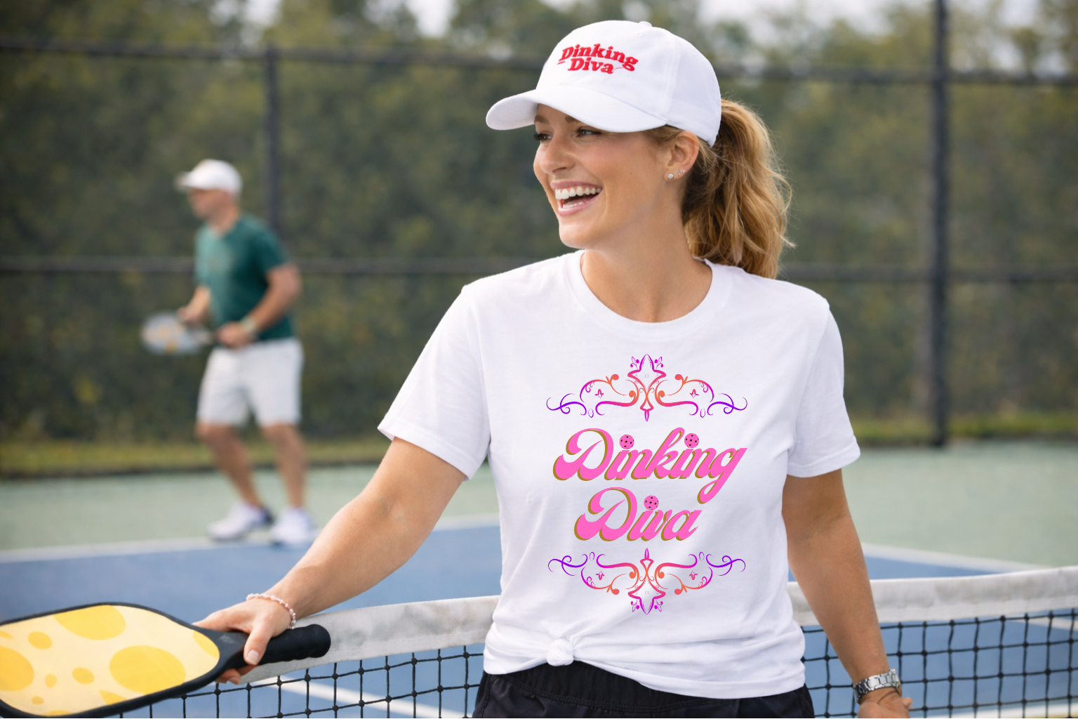 Woman on a tennis court wearing a 'Dinking Diva' shirt and cap.